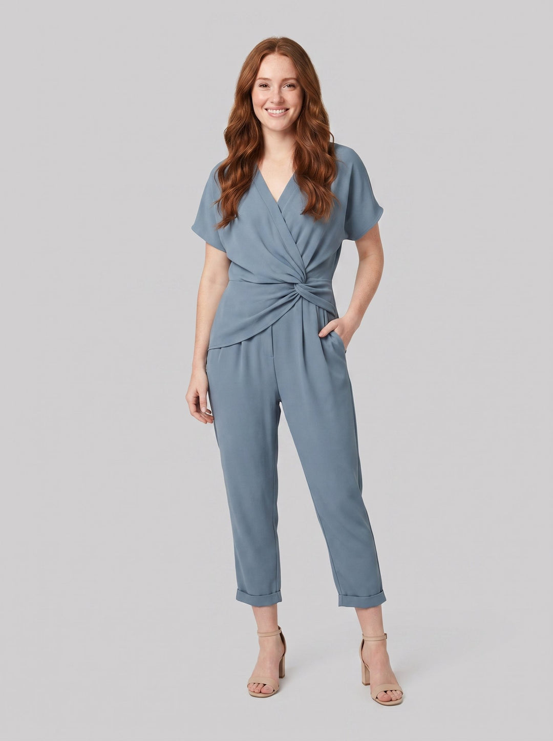 Lyra draped knot jumpsuit in dusty blue, wrap V-neck with knotted waist, front view on model